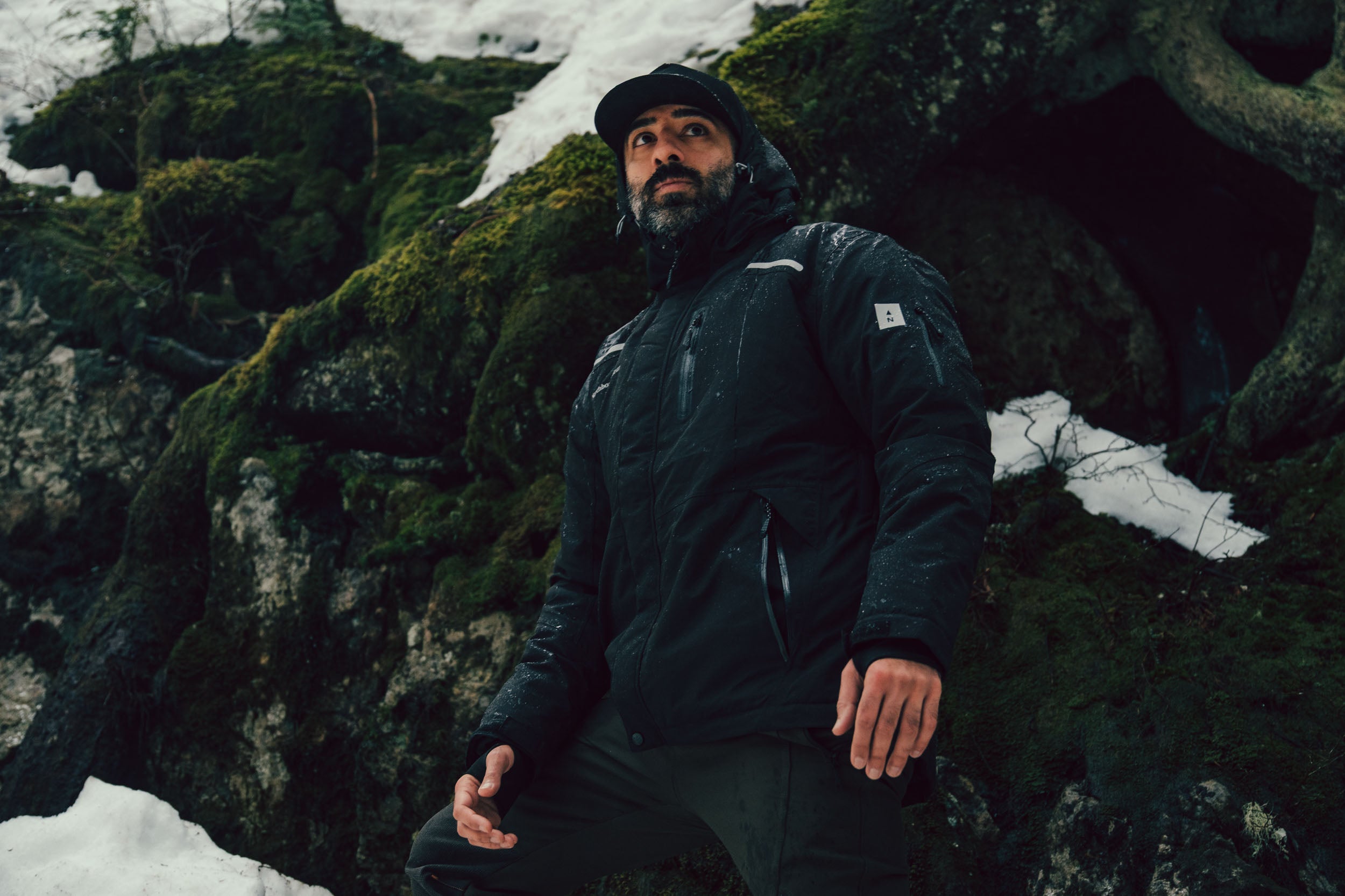 Man in a Northbound gear jacket sitting on a rocky, snowy landscape