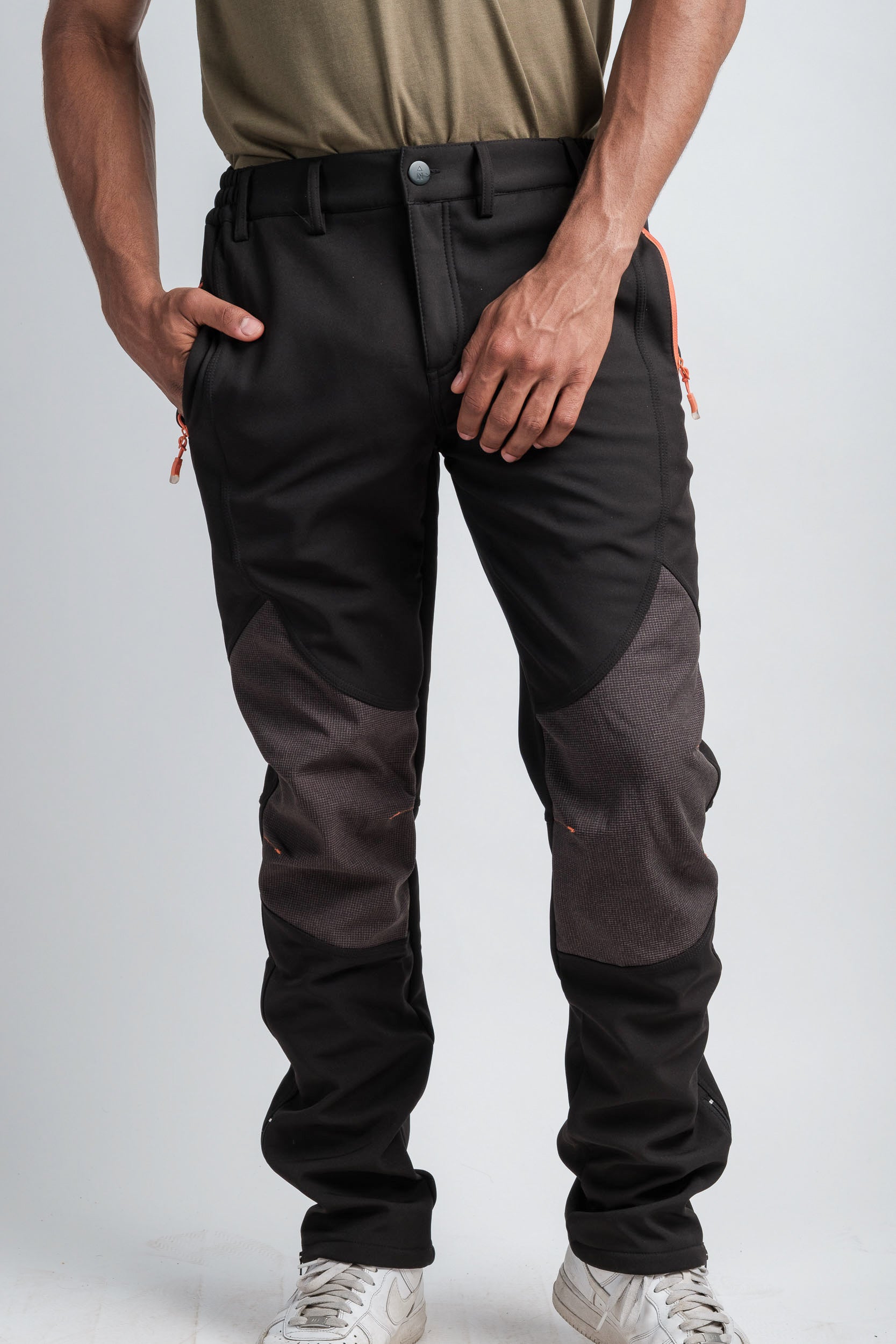 Northbound Gear men’s black outdoor pants with reinforced gray knee panels and orange zipper accents, shown in a studio setting.