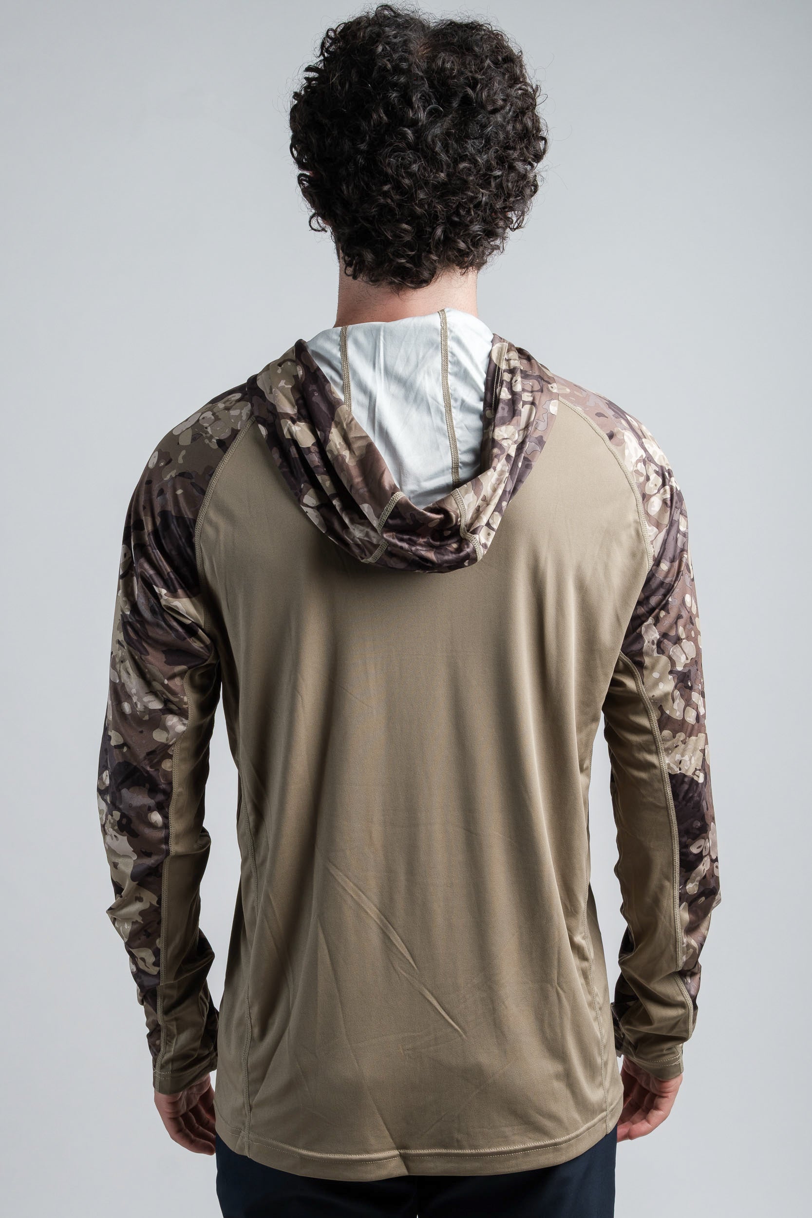 Person wearing a beige hoodie with camouflage sleeves on a plain background
